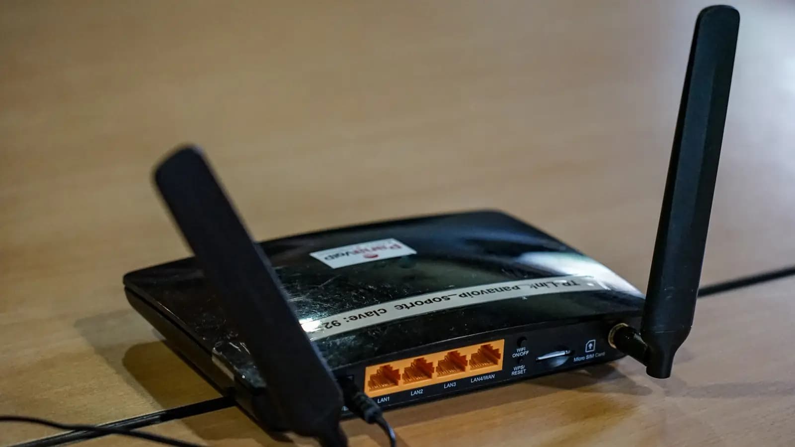 Parte traseira de um roteador Wi-Fi preto com antenas e portas LAN e WAN laranja