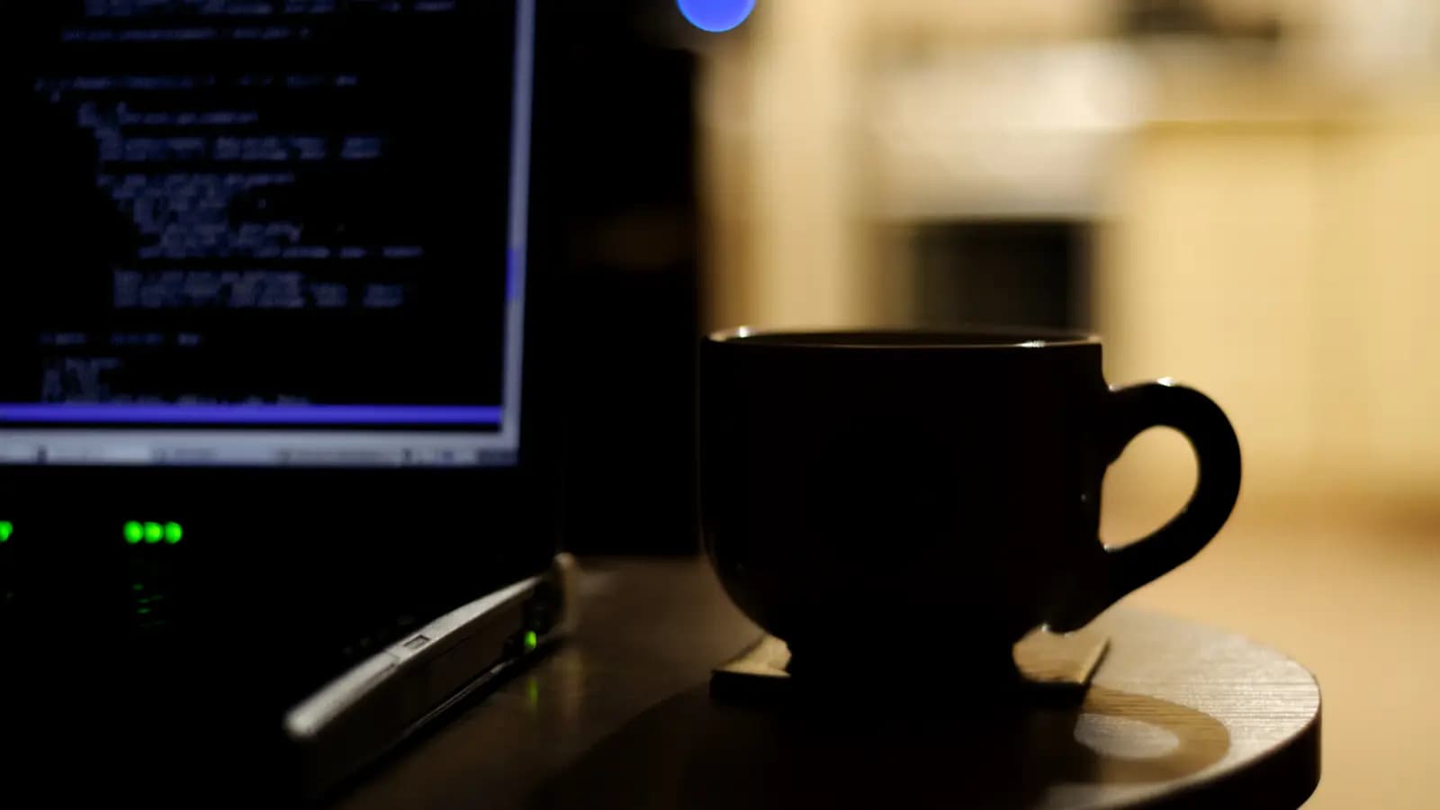 Tela de notebook com terminal de linhas de comando ao lado de uma xícara de café em ambiente escuro