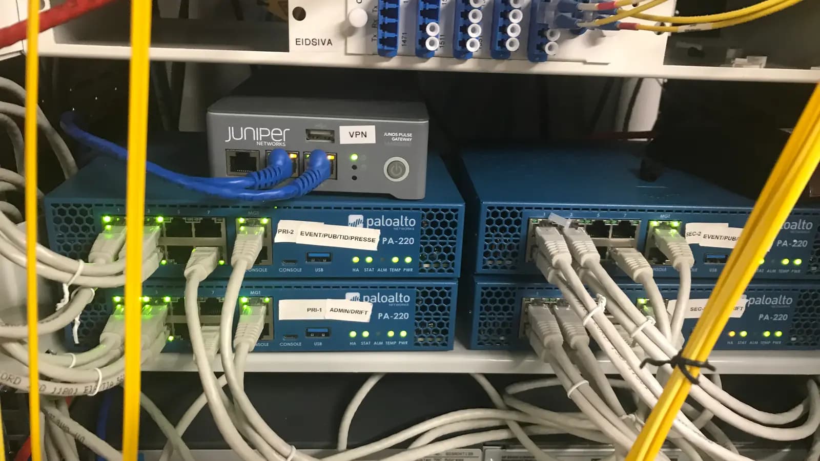 Firewalls Palo Alto azuis e gateway VPN Juniper em rack, conectados por diversos cabos de rede
