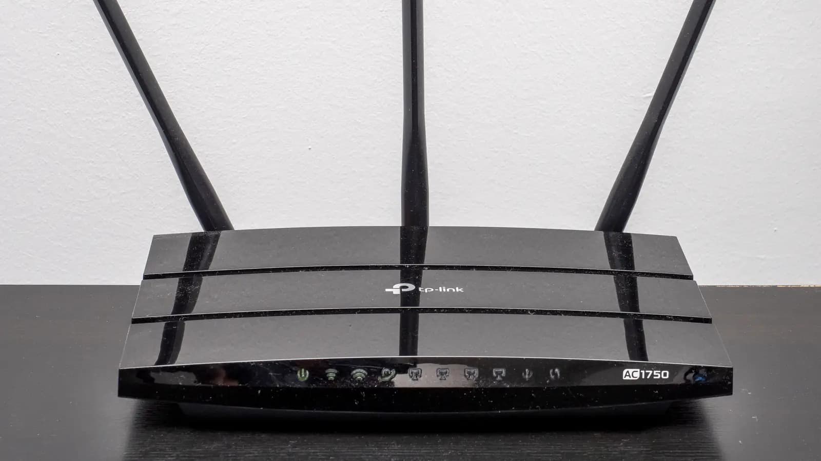 Roteador Wi-Fi preto com três antenas e luzes indicadoras no painel frontal sobre uma mesa