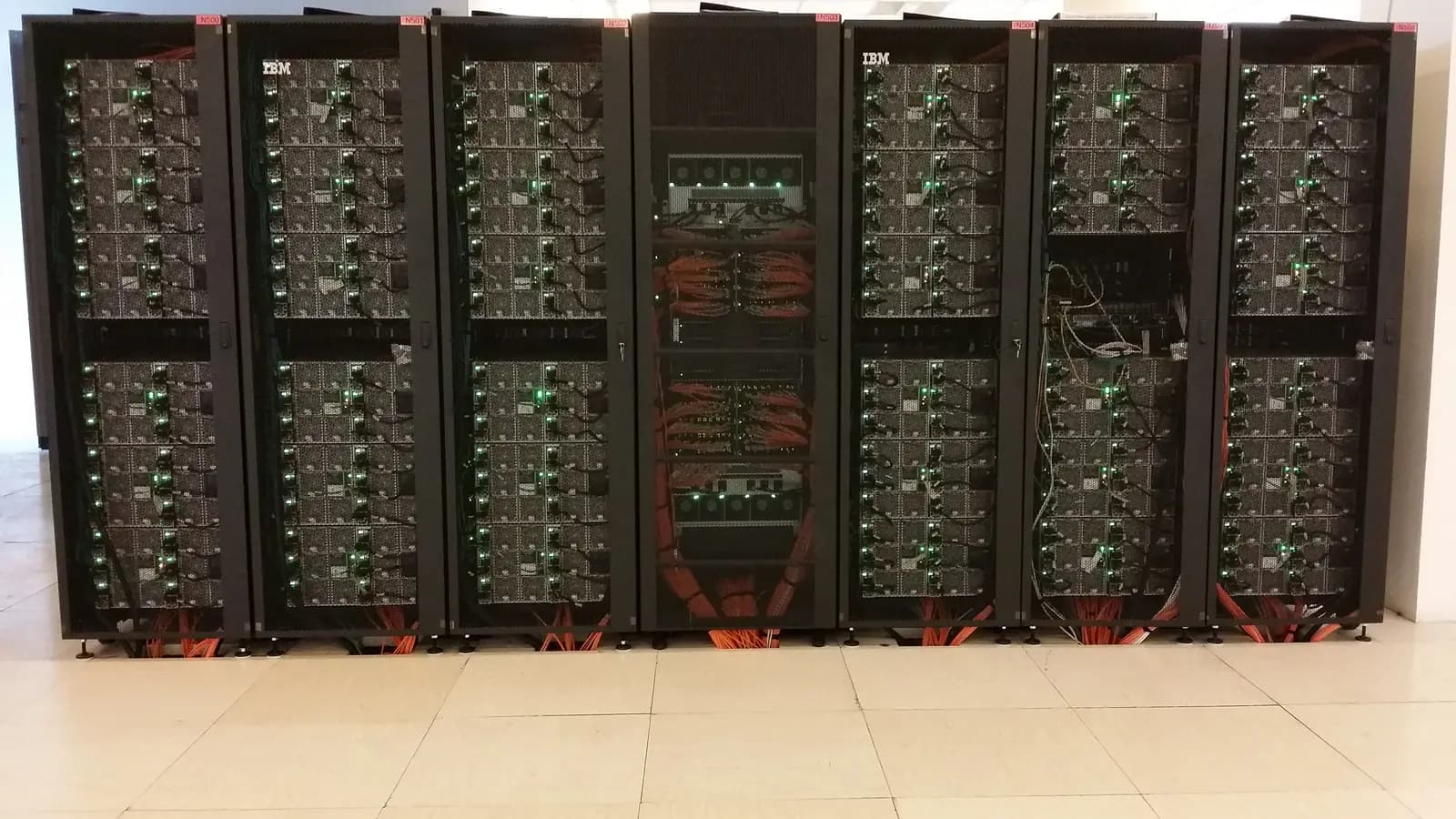 Fileira de racks de servidores com luzes verdes acesas e cabos laranja em um data center