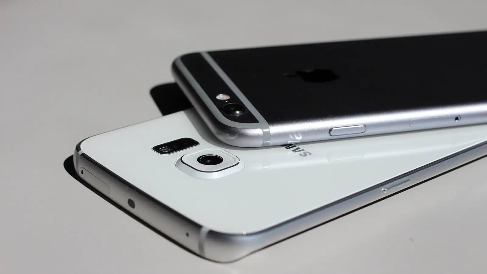 Smartphone Samsung Galaxy branco e iPhone preto empilhados sobre uma mesa clara