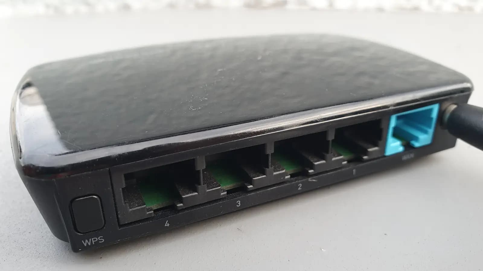 Parte traseira de um roteador Wi-Fi preto com quatro portas LAN e uma porta WAN azul