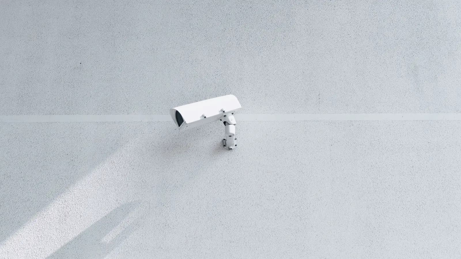 Câmera de vigilância branca fixada em uma parede clara, projetando sua sombra