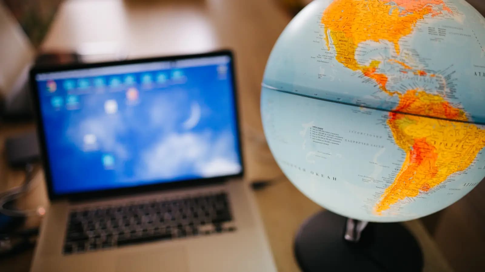 Globo terrestre mostrando as Américas em primeiro plano, com um notebook ligado desfocado ao fundo