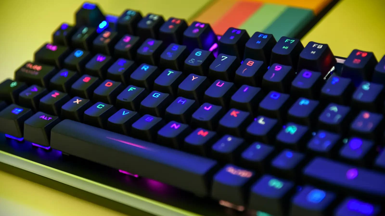 Teclado mecânico gamer com iluminação RGB colorida nas teclas, sobre uma mesa amarela